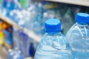 Butelki wody mineralnej z niebieskimi zakrętkami stoją na sklepowej półce.