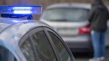 Fragment policyjnego radiowozu z włączonym niebieskim światłem na dachu, w tle rozmyty samochód.